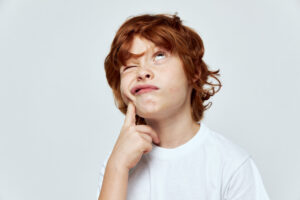 The red-haired boy looks upward is plotting something wrong white t-shirt gray background